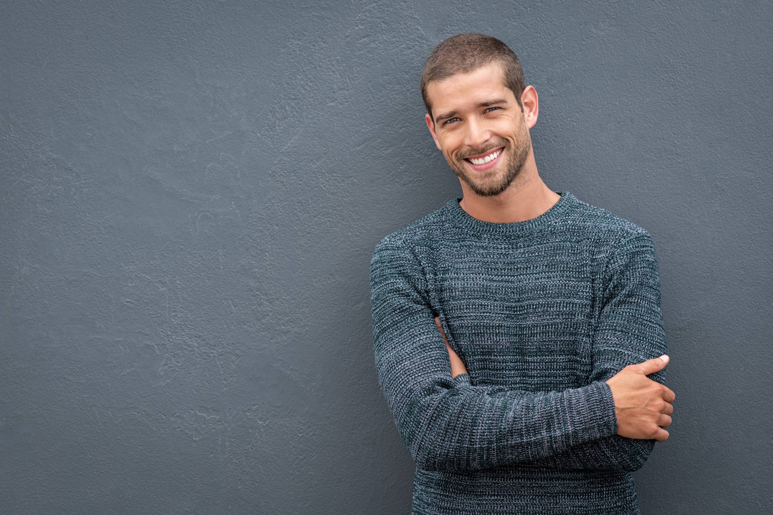 Homme souriant, croisant les bras, illustrant un beau sourire et une atmosphère accueillante du cabinet d'orthodontie.