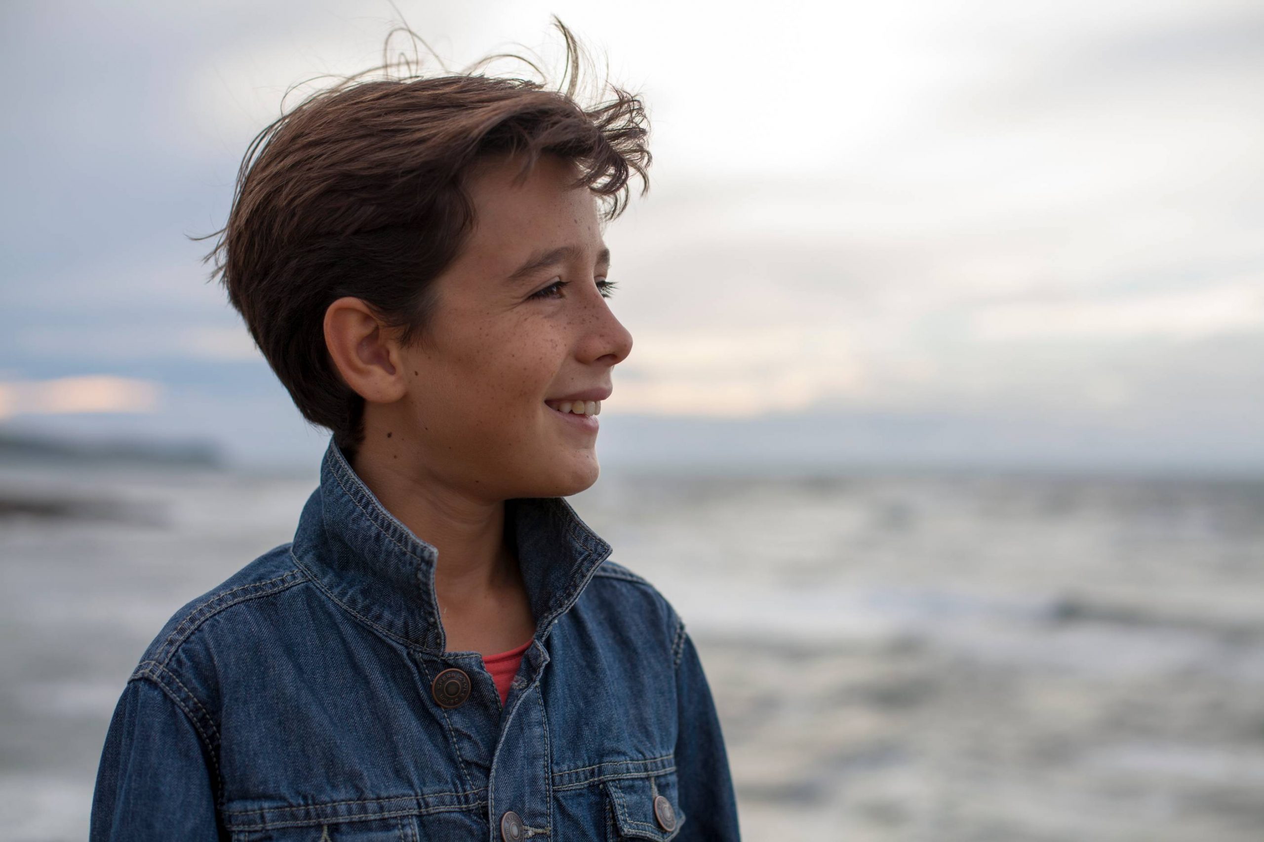Sourire heureux d'un jeune garçon face à la mer, illustrant l'importance des soins orthodontiques pour des sourires éclatants.