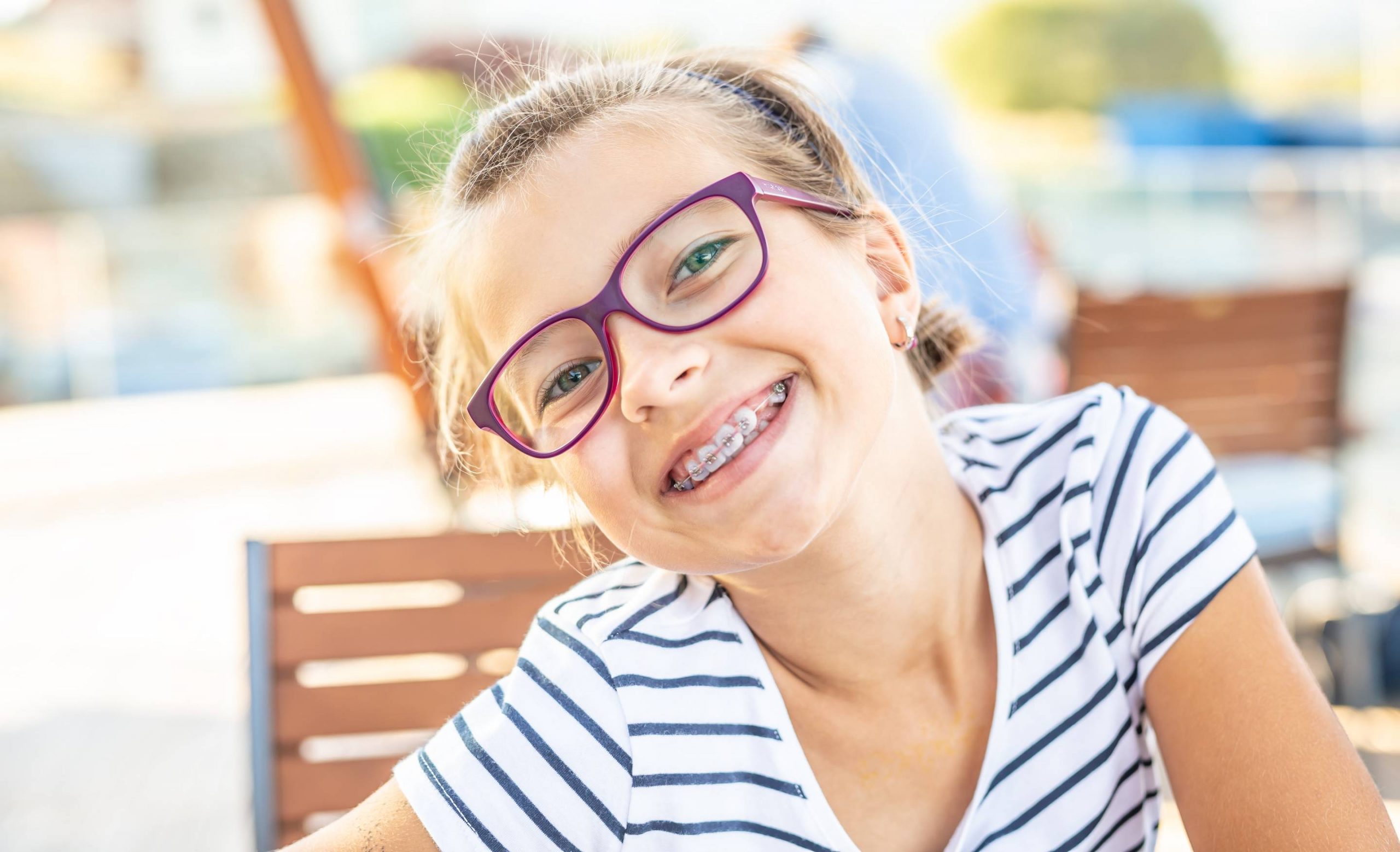 Fillette souriante portant des lunettes et un appareil dentaire, mettant en avant un beau sourire grâce aux soins orthodontiques.