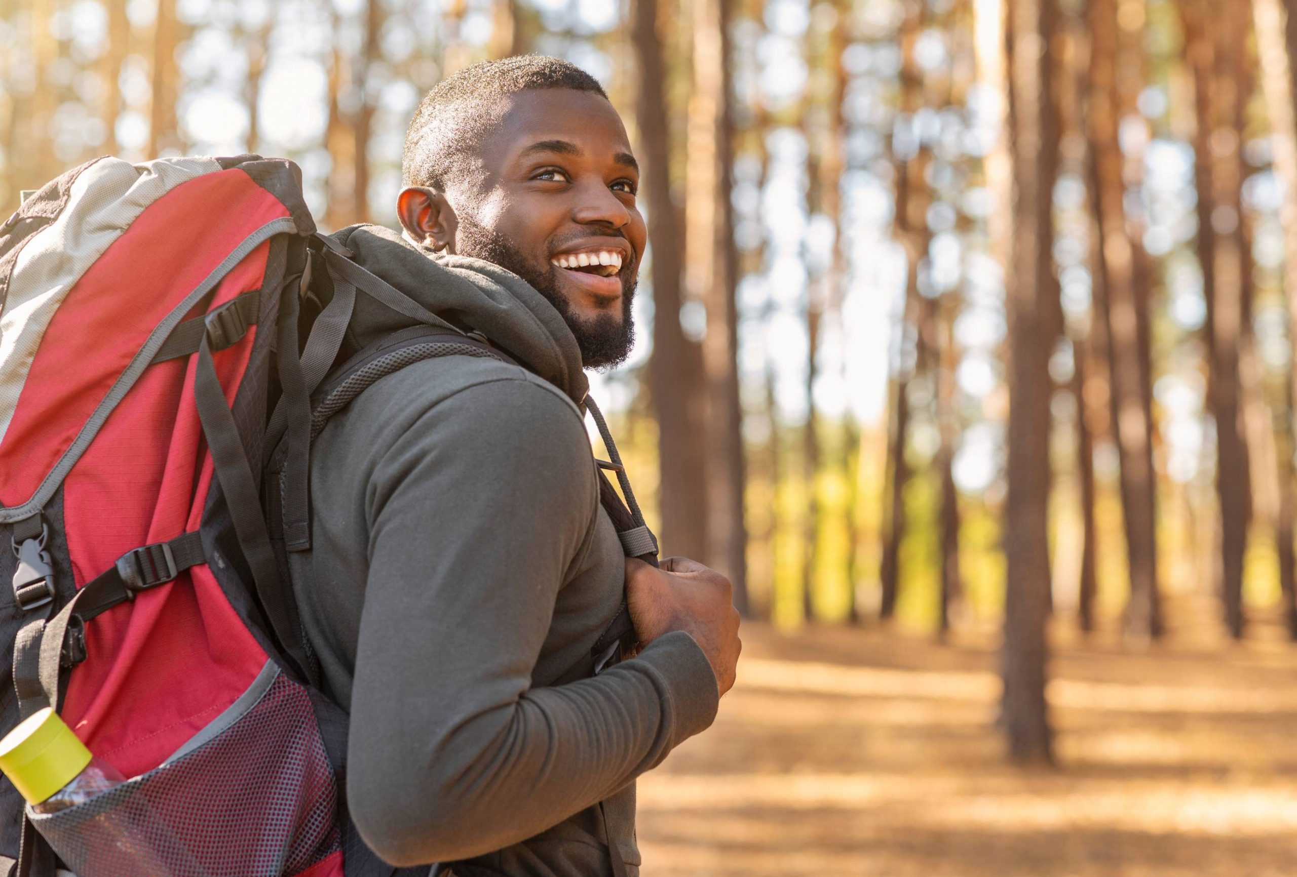 Homme souriant en pleine nature, portant un sac à dos, évoquant le plaisir des aventures et un sourire radieux.