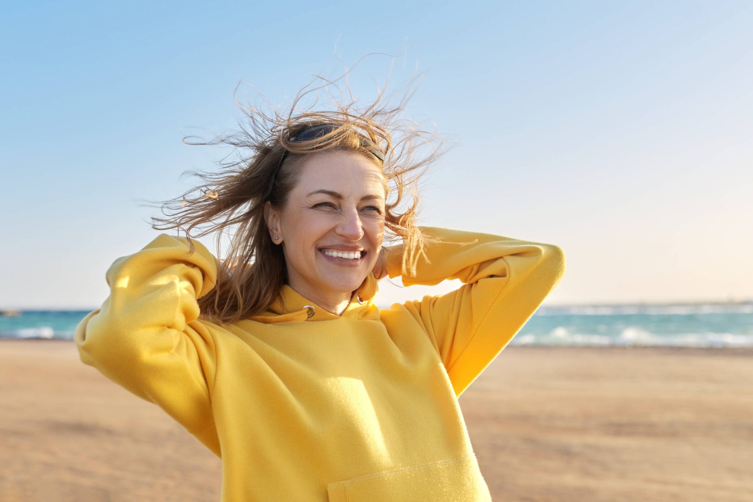 Femme souriante sur la plage, illustrant l’assurance d’un beau sourire grâce à des soins orthodontiques modernes.