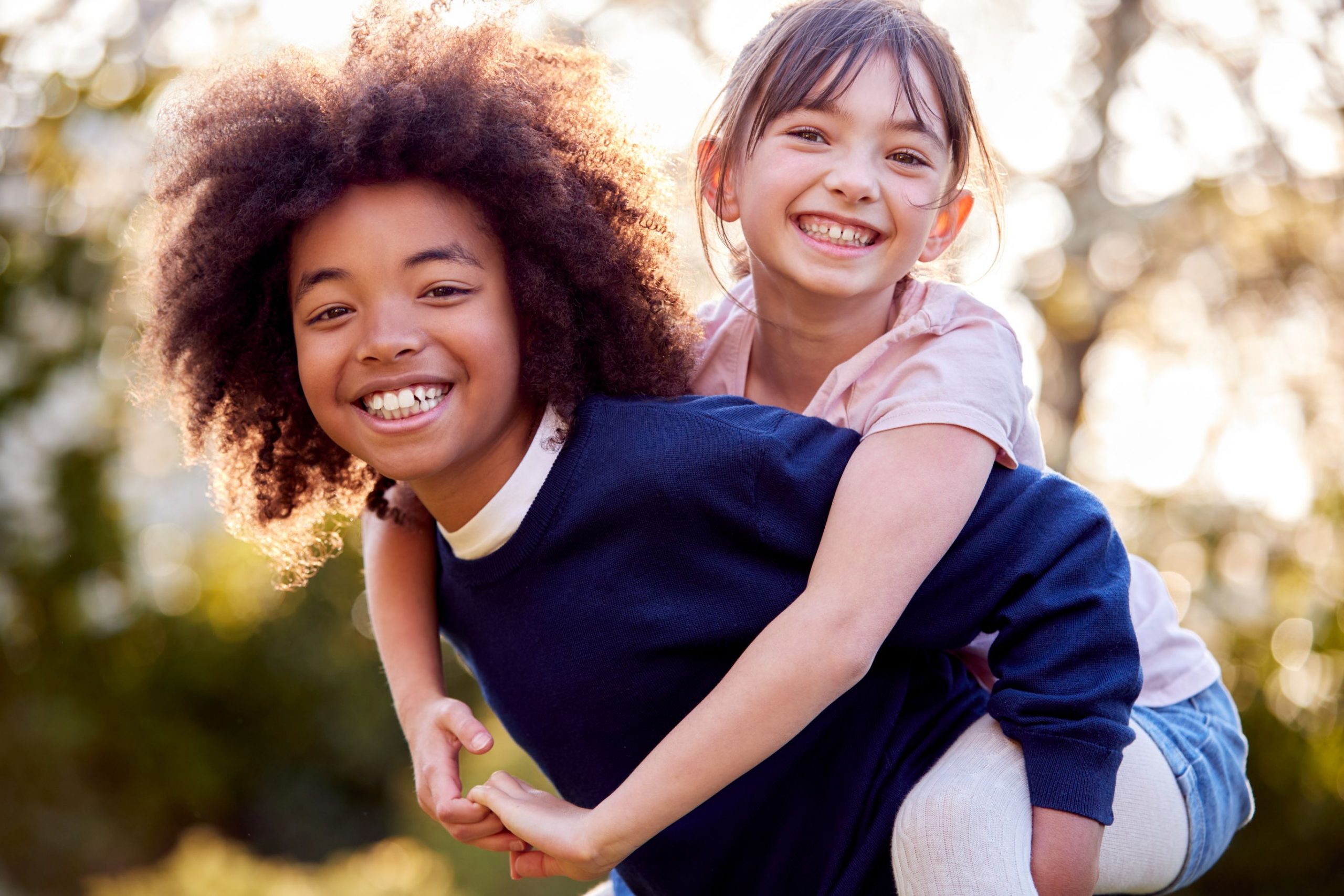 Deux enfants souriants, l'un portant l'autre sur son dos, illustrant la joie et la convivialité, reflet de soins orthodontiques attentionnés.